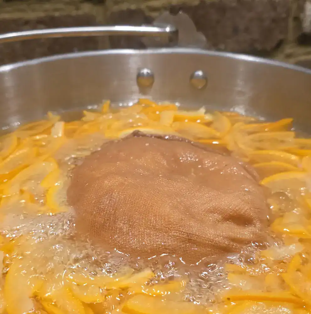 The pan of orange peel, boiling in water, with the muslin bag of pulp floating in the middle